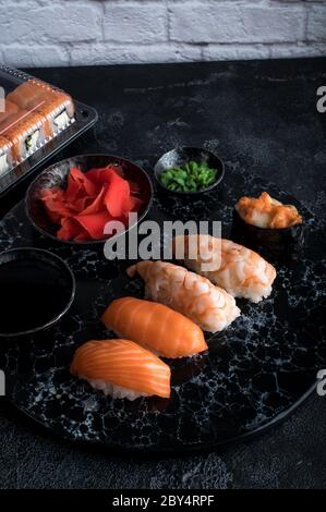 Délicieux sushi servi sur une ardoise en pierre sombre. Fond noir. Jeu de rouleaux de sushi dans une boîte en plastique, service de livraison Banque D'Images