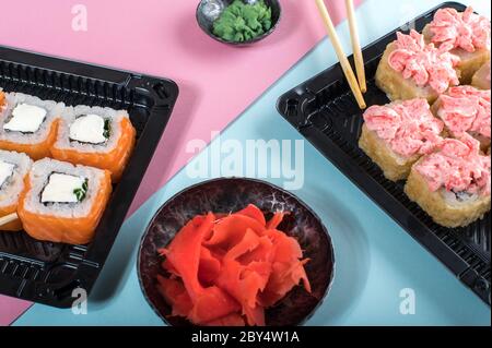 Assortiment de sushis servi dans des boîtes en plastique. Philadelphie et des rouleaux de lave. Livraison de nourriture. Arrière-plan rose et bleu Banque D'Images