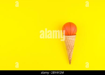 Ballon de basket-ball en forme de cône de gaufre crème glacée sur fond jaune, style minimaliste. Concept de divertissement sportif. Vue de dessus modèle d'espace de copie pour tex Banque D'Images