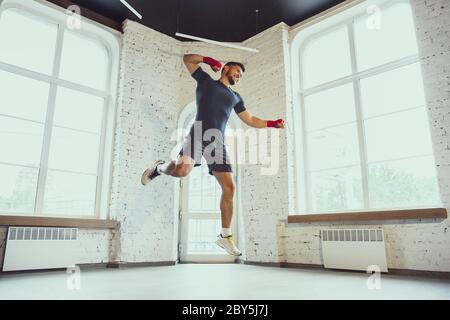 Sautez. Jeune homme caucasien s'entraîner à domicile pendant la quarantaine de l'épidémie de coronavirus, faisant des exercices de forme physique, Box. Rester sportif pendant l'isolation. Bien-être, sport, mouvement concept. Banque D'Images