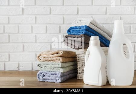 Concept de blanchisserie. Bouteilles avec gel détergent et serviettes luxuriantes dans le panier sur table en bois avec mur en brique blanche sur fond. Banque D'Images