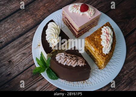 Collection de gâteaux divers sur fond de bois. Assortiment de morceaux de tranches avec crème. Assiette avec différents types de bonbons. Plusieurs tranches de délicieux desserts. Concept de menu de confiserie Banque D'Images