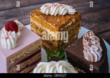 Collection de gâteaux divers sur fond de bois. Assortiment de morceaux de tranches avec crème. Assiette avec différents types de bonbons. Plusieurs tranches de délicieux desserts. Concept de menu de confiserie Banque D'Images