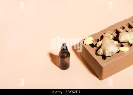Huile essentielle de gingembre biologique en bouteille de verre foncé, racine de gingembre et brique sur fond beige. Vue isométrique, espace de copie. Banque D'Images