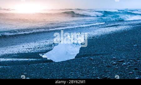 Les icebergs ont été écrasés par les vagues de la mer sur la plage noire au lever du soleil près du lac glacier de Jokulsarlon, en Islande. Banque D'Images