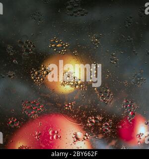 Gouttes magiques d'huile dissoutes dans l'eau sur un fond flou avec des fruits. Banque D'Images