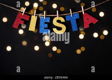 Fiesta Word fait de papier brillant et des épingles sur fond noir et des lumières de bokeh. Concept Cinco de mayo. Banque D'Images