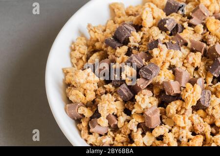 Granola croquante muesly avec des morceaux de chocolat noir et de lait dans un bol sur fond brun clair. Muesli dos. Vue de dessus. Macro. Copier l'espace. Banque D'Images