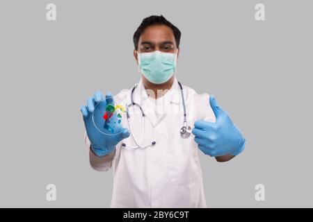 Médecin tenant une boîte de Petri portant un masque médical et des gants montrant le pouce vers le haut isolé. Médecine, concept de la science Banque D'Images