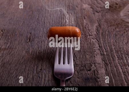 Saucisse fumée. Saucisse bouillie chaude sur une fourchette avec effet de vapeur sur une table en bois d'époque. Banque D'Images