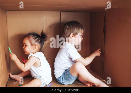 De beaux petits enfants dessinent avec des stylos-feutres et jouent dans la boîte, activité pour les enfants à la maison Banque D'Images