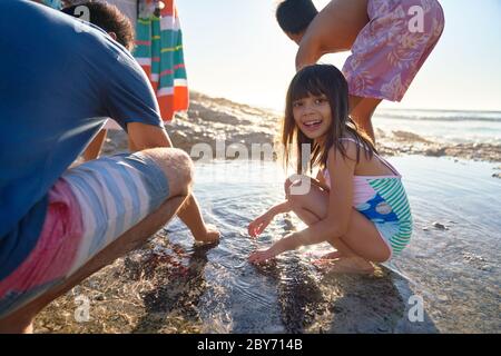 Portrait bonne fille jouant dans la piscine à marée avec la famille sur la plage ensoleillée