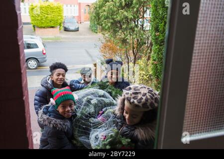 Une famille heureuse apporte un arbre de Noël à la porte d'entrée de la maison Banque D'Images