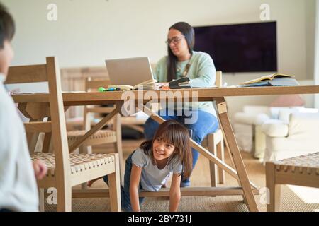 Enfants jouant sous la mère travaillant à la table à manger Banque D'Images