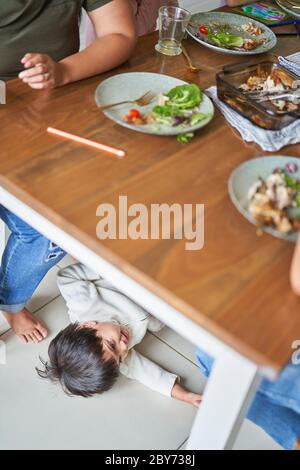 Garçon jouant sous une table de dîner Banque D'Images