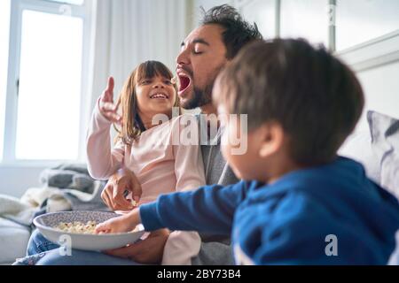 Les enfants jouent avec du pop-corn pour père sur le canapé Banque D'Images