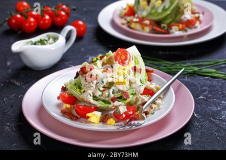 gros plan de la salade iceberg recouverte d'une vinaigrette au fromage bleu, bacon croustillant, tomates cerises, œufs durs, ciboulette sur des assiettes sur un béret Banque D'Images