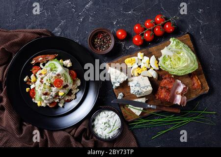 salade iceberg surmontée d'une vinaigrette au fromage bleu, bacon croustillant, tomates cerises, œufs durs émiettés, ciboulette sur des assiettes noires sur un conc Banque D'Images