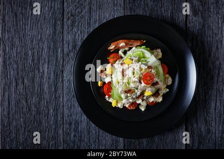 salade iceberg au fromage bleu, bacon croustillant, tomates cerises, œufs durs émiettés, ciboulette sur des assiettes noires à l'obscurité Banque D'Images