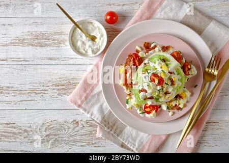 salade iceberg au fromage bleu, bacon croustillant, tomates cerises, œufs durs émiettés, ciboulette sur des assiettes roses sur un blanc Banque D'Images