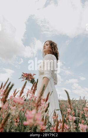 Portrait de jeune femme vêtu de blanc et portant des fleurs en regardant sur le côté Banque D'Images