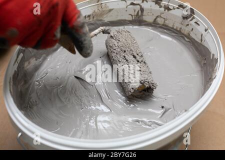 Un ouvrier de construction professionnel imbibe un rouleau de peinture dans un seau rempli d'isolation liquide d'humidité. Pendant le travail. Vue rapprochée. Banque D'Images