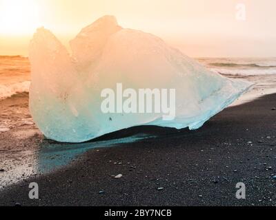 Les icebergs ont été écrasés par les vagues de la mer sur la plage noire au lever du soleil près du lac glacier de Jokulsarlon, en Islande. Banque D'Images