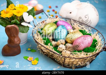 Printemps Pâques pour les vacances. Composition de Pâques avec œufs de Pâques colorés sur mousse dans le panier, le lapin et le pot de fleurs de printemps. Vue de dessus Banque D'Images