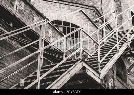 Escaliers extérieurs métalliques d'une ancienne usine de textile abandonnée en noir et blanc Banque D'Images