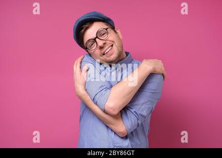 Heureux caucasiens homme se hous lui-même, a une grande estime de soi, a un sourire en dents de souris. Studio tourné sur un mur rose. Banque D'Images