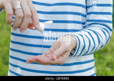 une femme verse un gel désinfectant transparent pour les mains sur une paume à partir d'une petite bouteille à l'extérieur sur un fond vert Banque D'Images