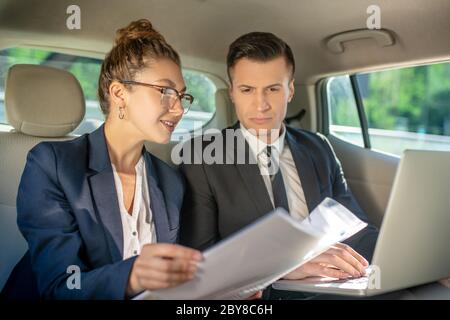 Femme en lunettes avec documents et homme avec un ordinateur portable. Banque D'Images