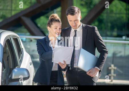 Femme avec des papiers et homme avec un ordinateur portable près de la voiture Banque D'Images