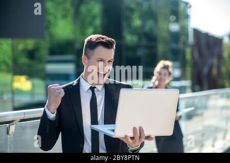 Jeune homme avec un ordinateur portable se réjouit avec enthousiasme Banque D'Images