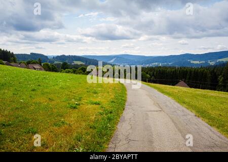 Panorama pittoresque avec route déserte entre les prairies en pente dans le paysage de la haute Forêt Noire à Breitnau, Bade-Wurtemberg, Allemagne sur un ciel nuageux Banque D'Images