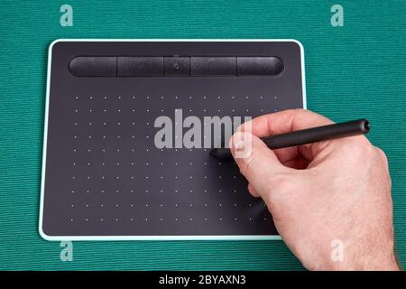 La main de l'artiste tient un stylet ou un stylet sur l'écran d'une tablette graphique, il s'agit d'un périphérique de saisie lors de l'utilisation de programmes de traitement d'image. Photographie Banque D'Images