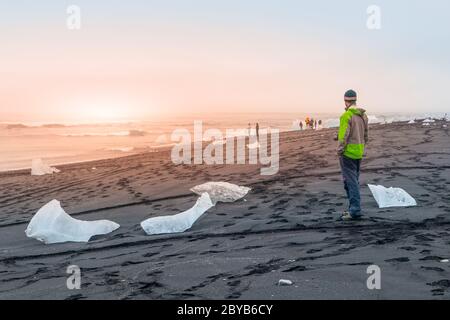 Morceaux de glace sur sable noir, détail naturel, Islande. Homme debout sur la plage noire. Banque D'Images