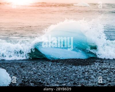 Les icebergs ont été écrasés par les vagues de la mer sur la plage noire au lever du soleil près du lac glacier de Jokulsarlon, en Islande. Banque D'Images