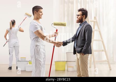 Peintre masculin se secouant la main avec un homme barbu et une peintre féminine peignant un mur à l'intérieur d'une maison Banque D'Images