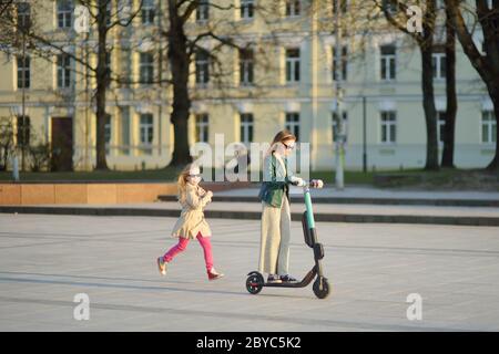 Jolie jeune fille à cheval électrique le jour chaud et ensoleillé du printemps. Transport urbain électrique à Vilnius, Lituanie. Location de scooters. Famil Banque D'Images