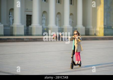 Jolie jeune fille à cheval électrique le jour chaud et ensoleillé du printemps. Transport urbain électrique à Vilnius, Lituanie. Location de scooters. Famil Banque D'Images