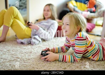 Deux sœurs jouant à des jeux vidéo à la maison. Les enfants qui s'amusent ensemble détiennent des contrôleurs de jeu. Loisirs en famille et plaisir à l'intérieur. Banque D'Images