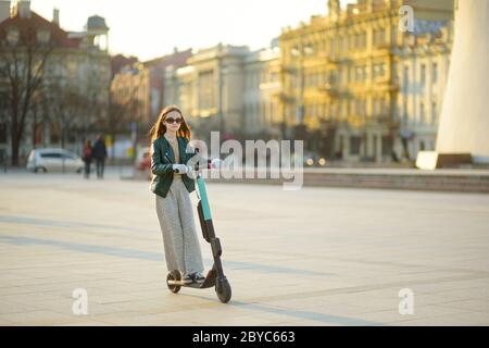 Jolie jeune fille à cheval électrique le jour chaud et ensoleillé du printemps. Transport urbain électrique à Vilnius, Lituanie. Location de scooters. Famil Banque D'Images