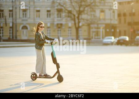 Jolie jeune fille à cheval électrique le jour chaud et ensoleillé du printemps. Transport urbain électrique à Vilnius, Lituanie. Location de scooters. Famil Banque D'Images