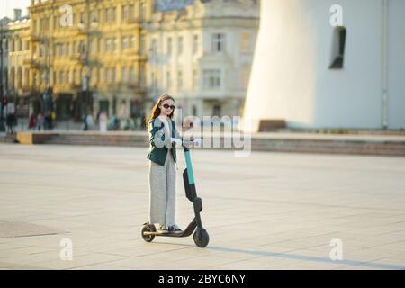 Jolie jeune fille à cheval électrique le jour chaud et ensoleillé du printemps. Transport urbain électrique à Vilnius, Lituanie. Location de scooters. Famil Banque D'Images