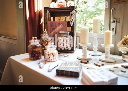 Barre de bonbons de plusieurs sortes de bonbons colorés dans des pots en verre décorés de bougies sur table habillée blanche. Concept mariage ou fête. Banque D'Images