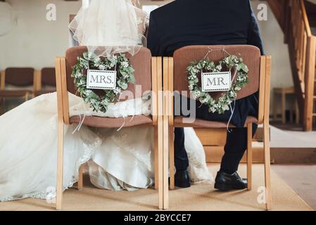 Vue arrière du couple assis sur des chaises décorées de coeurs de fleurs et de tables M. et Mme Bonde et marié à la cérémonie de mariage. Concept de jour de wadding. Banque D'Images