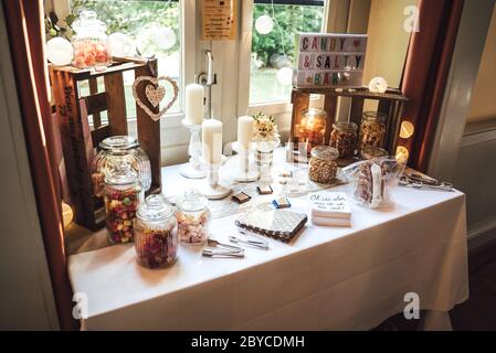 Salées et barre de bonbons de plusieurs sortes de collations salées et de bonbons colorés dans des pots en verre décorés de bougies sur table habillée blanche.mariage ou fête Banque D'Images