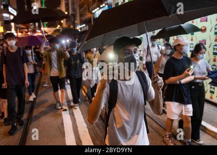 Des manifestants pro-démocratie se promondent dans les rues en portant un masque facial et en tenant des parasols pour commémorer le premier anniversaire du mouvement anti-extradition.des manifestants pro-démocratie sont descendus dans les rues pour marquer le premier anniversaire du mouvement anti-extradition dans le district central de Hong Kong. Banque D'Images