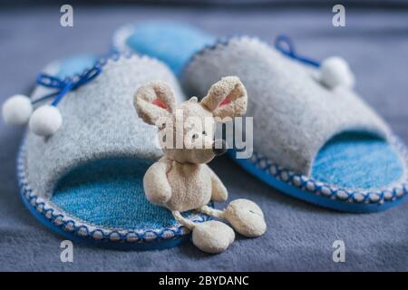 Une souris de jouet est assise sur des chaussons avec pompons debout sur un tapis moelleux. Vêtements et chaussures pour femmes ou enfants. Le concept de la chaleur à la maison. Banque D'Images